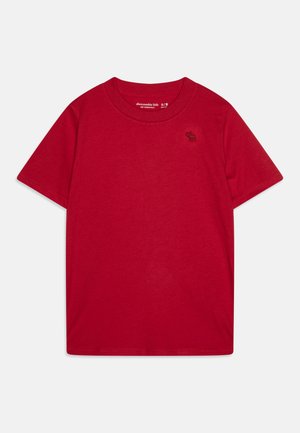Camiseta de algodón roja con mangas cortas, cuello redondo y pequeño logo negro en el lado izquierdo del pecho. Tela suave y ligera con una textura lisa.