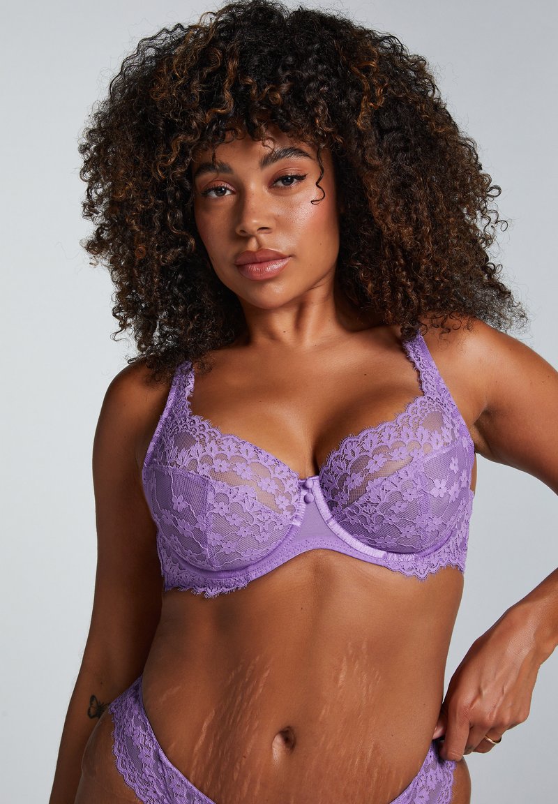 Lila spetsbh med byglar, prydd med blommönster, justerbara band och en liten slinga framtill. Slät, texturerad tyg.