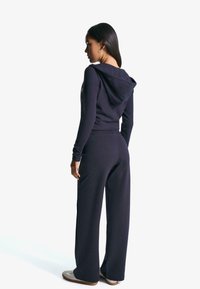 Námornícky dvojdielny lounge set vyrobený z mäkkej tkaniny, pozostávajúci z krátkeho hoodie a širokých nohavíc, s voľným strihom a jemnými šitými detailmi.