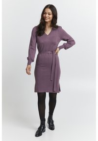 Abito in maglia color malva con scollatura a V, maniche lunghe, vita arricciata e spacchi laterali. Abbinato a stivali neri alla caviglia e collant.