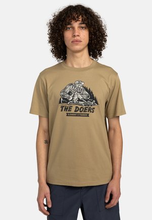 Camiseta de algodón color marrón con un diseño gráfico negro que presenta a un leñador y árboles. Manga corta, cuello redondo, corte estándar.