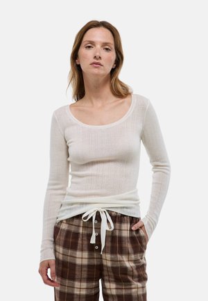 Haut à manches longues en maille ribbed blanc cassé avec un grand décolleté en cœur, associé à un pantalon à carreaux marron avec cordon de serrage et fermeture à bouton.