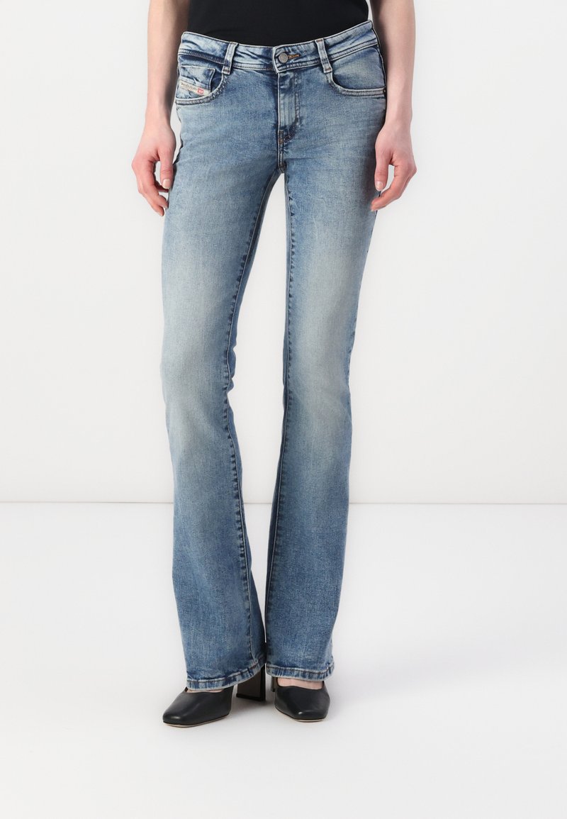 Blugi evazați de culoare albastru deschis, din denim. Au o talie medie, ușor decolorată și detalii de cusătură pe buzunare. Asortați cu pantofi cu toc negri.