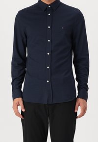 Camisa azul marino abotonada con un patrón texturizado de espina de pescado, mangas largas, cuello puntiagudo y botones blancos, diseñada con un corte ajustado.