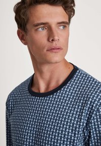 Langsleeve overhemd met een marineblauw geometrisch patroon en een contrasterende marineblauwe ronde hals. De stof lijkt zacht met een gladde textuur.