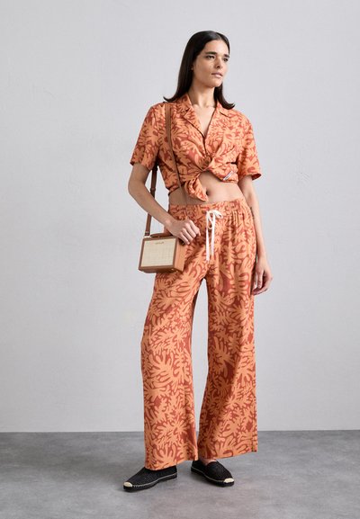 Cropped shirt and wide-leg pants set in orange with a leaf pattern. Accessories include a small bag with a wood detail and black espadrilles.