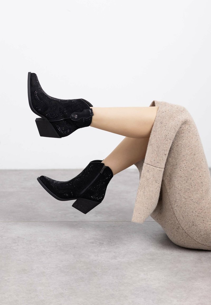 Botines de ante negros con un patrón texturizado, punta redondeada y tacón cuadrado. Tienen un zipper lateral y botones decorativos.