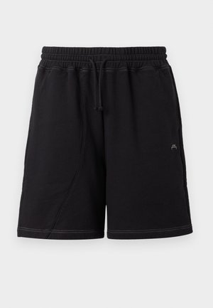 Mees kannab valget graafilise mustriga t-särki, musti lühikesi pükse, musti sokke ja vabaajajalatsid, kandes suurt halli õlakotti ühetoonilise heleda tausta ees.