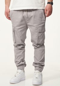 Helle graue Cargo-Hosen mit elastischen Bündchen, Vorder- und Seitentaschen, Kordelzugbund aus weichem Stoff. Getragen mit weißen Turnschuhen.