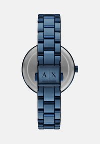 Modra kovinska zapestnica s povezanim pasom in okroglo številčnico. Ima minimalističen dizajn in vgravirano logo na zapirali. Srebrni detajli na številčnici.