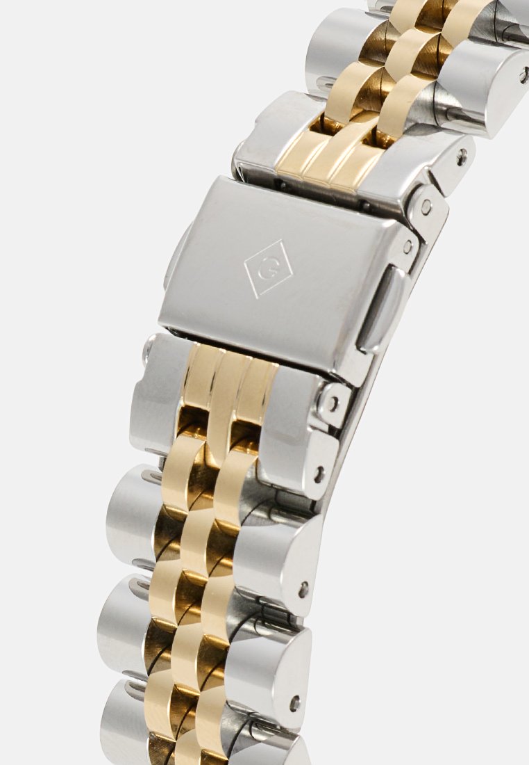 Bracelet de montre en acier inoxydable argenté et doré avec des maillons entrelacés, présentant une finition brossée, un fermoir déployant et une texture lisse.