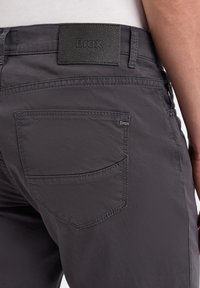 Grijze broek van een gladde stof met een achterzak met gedetailleerde stiksels en een leren logo patch op de tailleband.