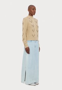 Beige kudumisega särk, millel on teemantmuster, koos helesinise denimpikkade seeliku, millel on külgslitt, kantud hõbedaste kingadega.