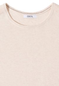 Pull beige col rond avec une étiquette de marque "CECIL" cousue à l'intérieur de l'encolure sur fond blanc.