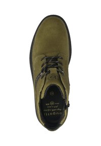 Olivgrüner Wildlederknöchelschuh mit schwarzen Schnürsenkeln, strukturierter Oberfläche und kontrastierender dunkler Sohle. Innenbereich enthält Branding-Details und Größe.