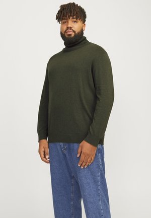 Suéter de cuello alto verde oscuro en tela suave, con mangas largas y un ajuste relajado, combinado con jeans de denim azul claro.