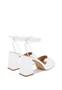 Sandali bianchi con tacco a blocco, punta aperta e lacci alla caviglia. Materiale morbido e design minimalista con soletta color cuoio.