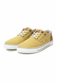 Zapatillas de lona amarillas con suelas de goma blanca, con cordones beige, detalles de cuero en el talón y detalles a rayas en blanco y negro.