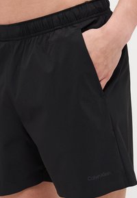 Juodi maudymosi šortai su elastinga juosmeniu, šoninėmis kišenėmis ir subtiliu Calvin Klein logotipu. Lygi, lengva medžiaga.