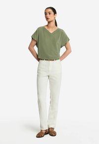 Olivgrön v-halsad blus, avslappnad passform, tillsammans med vita raka byxor och bruna sandalettar med remmar, framhävd av ett smalt bälte.