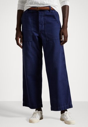 Navy blue wide-leg trousers made of denim with front patch pockets, paired with a braided brown belt and white sneakers.