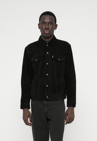 Μαύρο τζάκετ από σουέτ τζιν με γιακά, μπροστινές τσέπες, κλείσιμο με κουμπί και αντίθετη ραφή, συνδυασμένο με σκούρα τζιν.