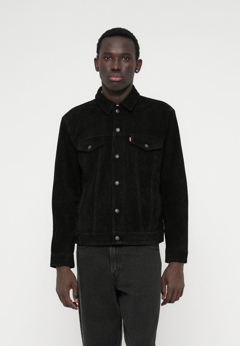 Μαύρο τζάκετ από σουέτ τζιν με γιακά, μπροστινές τσέπες, κλείσιμο με κουμπί και αντίθετη ραφή, συνδυασμένο με σκούρα τζιν.