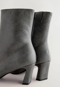 Grå læder ankelstøvler med en struktureret overflade, der har en spids form og en kraftig hæl. Indeholder synlige stikninger.
