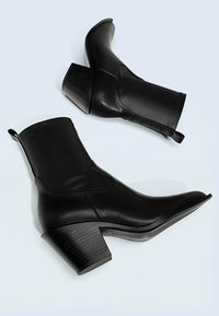Botas de tobillo de cuero negro con tacón de bloque acanalado, punta afilada y acentos bordados, con tiradores traseros para facilitar su puesta.