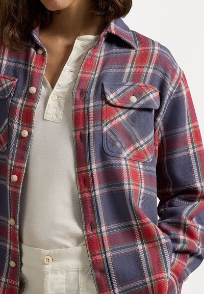 Checked flannel shirt in navy, red, and white, featuring a button-up front, collar, and one chest pocket. Worn over a white top.