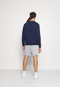 Sweatshirt marine à col rond, avec des poignets et un ourlet côtelés, associé à un short gris clair. Des baskets blanches complètent la tenue.