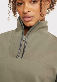 Suéter verde oliva con cuello alto, con media cremallera, textura suave y detalles de costura en tonos. Diseño casual y cómodo.
