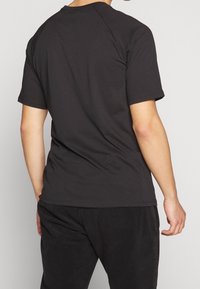 Musta puuvillainen t-paita pyöreällä pääntiellä ja lyhyillä hihoilla, jossa on sileä pinta ja rento istuvuus, nähtynä takaa.