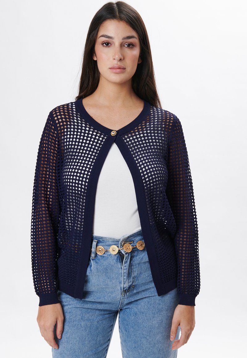 Navyblaue Strickjacke mit offenem Mesh-Design, Rundhalsausschnitt und einem einzelnen goldenen Knopfverschluss. Lange Ärmel mit gerippten Bündchen.