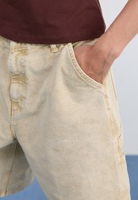 Beige denimshorts med sidofickor, med en avslappnad passform och lätt skrynklor, tillsammans med en mörkröd t-shirt med rund halsringning.