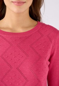 Fuchsia gebreide trui met een ronde halslijn, getextureerde geometrische patronen en kleine stipversieringen. Gladde oppervlakte-textuur.