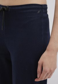 Navy blue joggers in soft denim material, featuring an elastic waistband with a drawstring and a small logo on the side. Smooth texture.