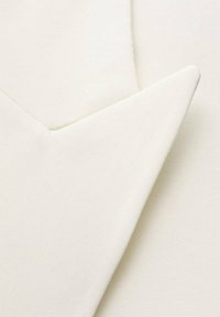 Tessuto color crema con una superficie strutturata, caratterizzato da un angolo netto e un bordo piegato, che presenta un design liscio e pulito.