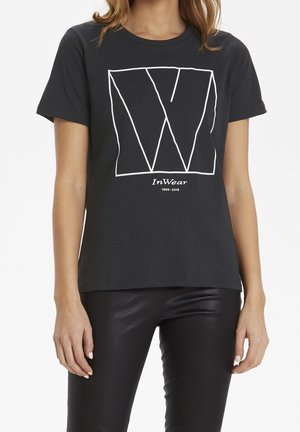 Schwarzes Baumwoll-T-Shirt mit einem auffälligen weißen geometrischen Buchstaben "W", der zentriert auf der Vorderseite angebracht ist. Mit kurzen Ärmeln und Rundhalsausschnitt.