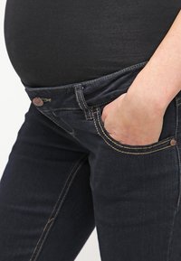 Jeans för gravida i mörkblått med gul sömnad, slim fit, med knappstängning och framfickor. Mjukt, elastiskt material.