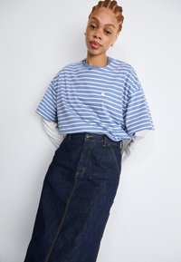 T-shirt a righe blu con scollatura rotonda, sovrapposto a una maglietta bianca a maniche lunghe, abbinato a una gonna a tubino in denim scuro.