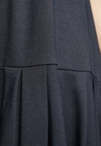 Tissu plissé bleu foncé avec une finition texturée, présentant une couture au-dessus des plis. Léger et tombe doucement.