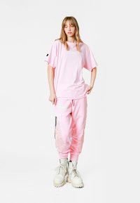 Camiseta rosa oversized con un parche y pantalones de chándal rosa a juego con bordado, combinados con botas blancas de cordones.
