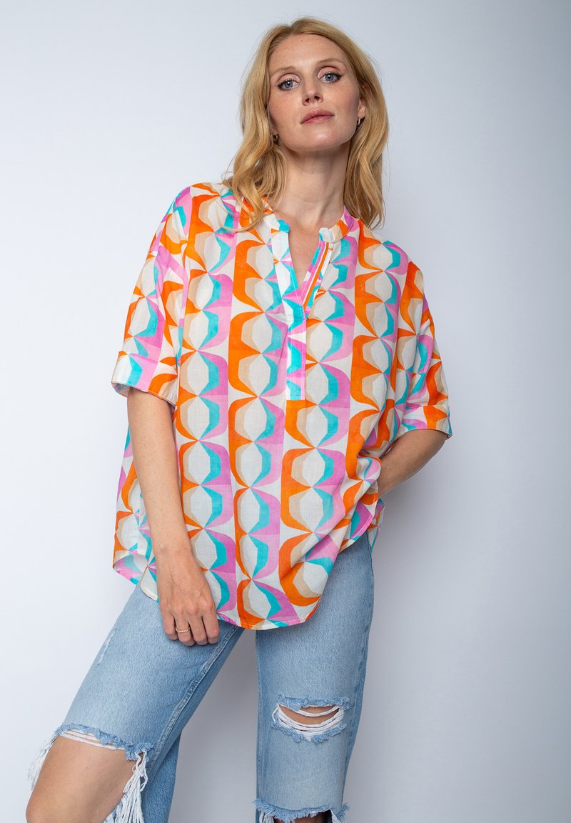 Kolorowa, wzorzysta bluzka z krótkim rękawem i kołnierzykiem mandarynkowym. Oferuje geometryczne kształty w kolorach pomarańczowym, różowym, niebieskim i białym na lekkim materiale.