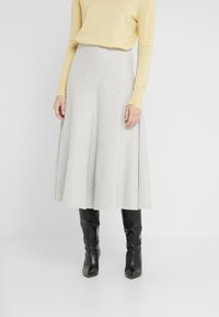 Jasnoszara, do kolan, rozkloszowana spódnica z miękkiego materiału, o gładkiej strukturze i wysokim stanie, zestawiona z żółtą bluzką z długim rękawem i czarnymi botkami.