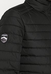 Chaqueta de plumas negra con costuras horizontales, cuello alto y parche de logo bordado en el hombro izquierdo. Tejido texturizado e insulated.