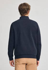 Marineblauwe sweatshirt met een hoge kraag, geribbelde manchetten en zoom. Gemaakt van zacht materiaal, met een minimalistisch ontwerp en zonder zichtbare logo's.