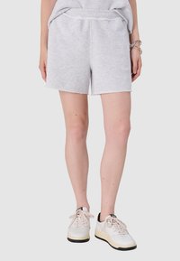 Jasnoszare bawełniane szorty z elastycznym pasem i postrzępionym dołem, w połączeniu z białymi i czarnymi trampkami, wyposażonymi w sznurowania oraz teksturowe detale.