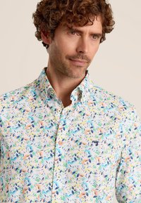 Geknoopte blouse met een levendig bloemenpatroon in pastelkleuren, gemaakt van lichtgewicht stof met een standaard kraag en een klein logodetail.