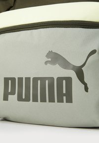 Groene stoffen zak met een zachte, lichtgele bovenkant. Bevat een groot, donkergrijs "PUMA" logo en een springende poema grafiek. Met ritsluiting.